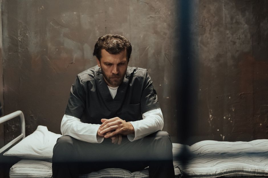 A solitary prisoner in deep thought, sitting on a cell bed inside a prison.